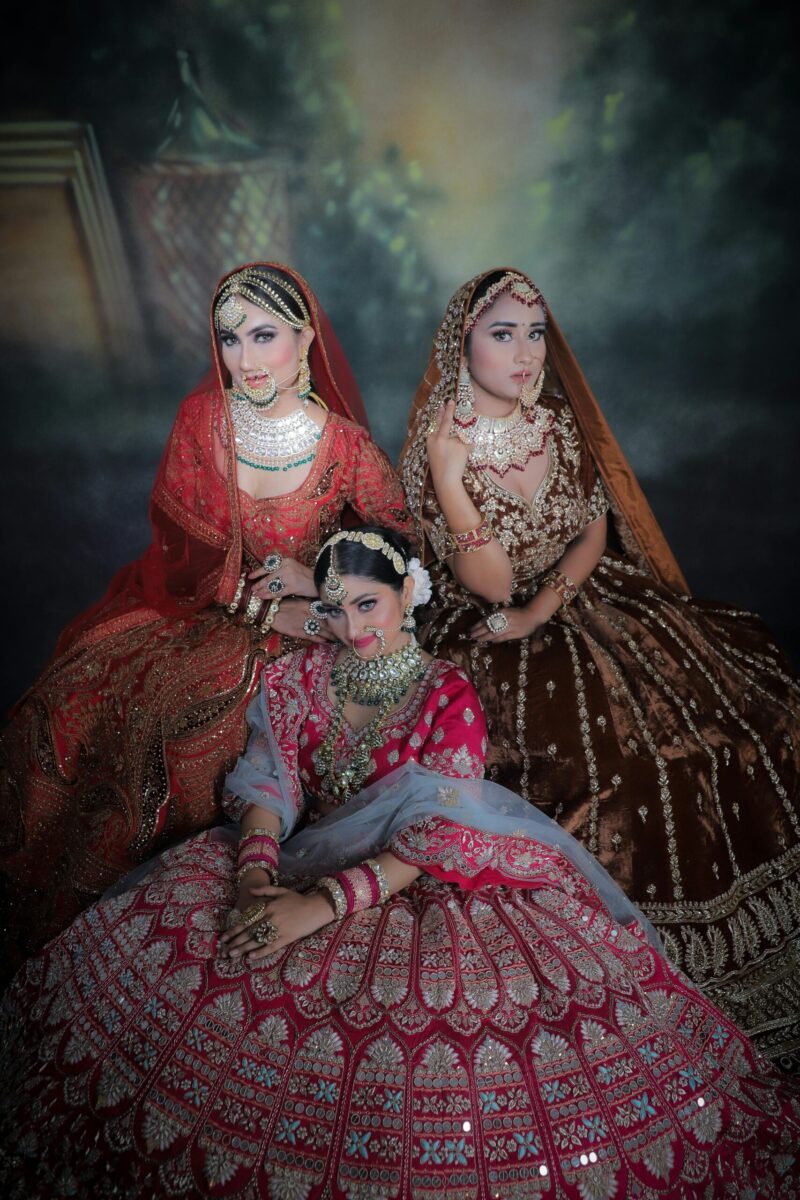 Three women in traditional lehengas, adorned with jewelry, striking elegant poses.