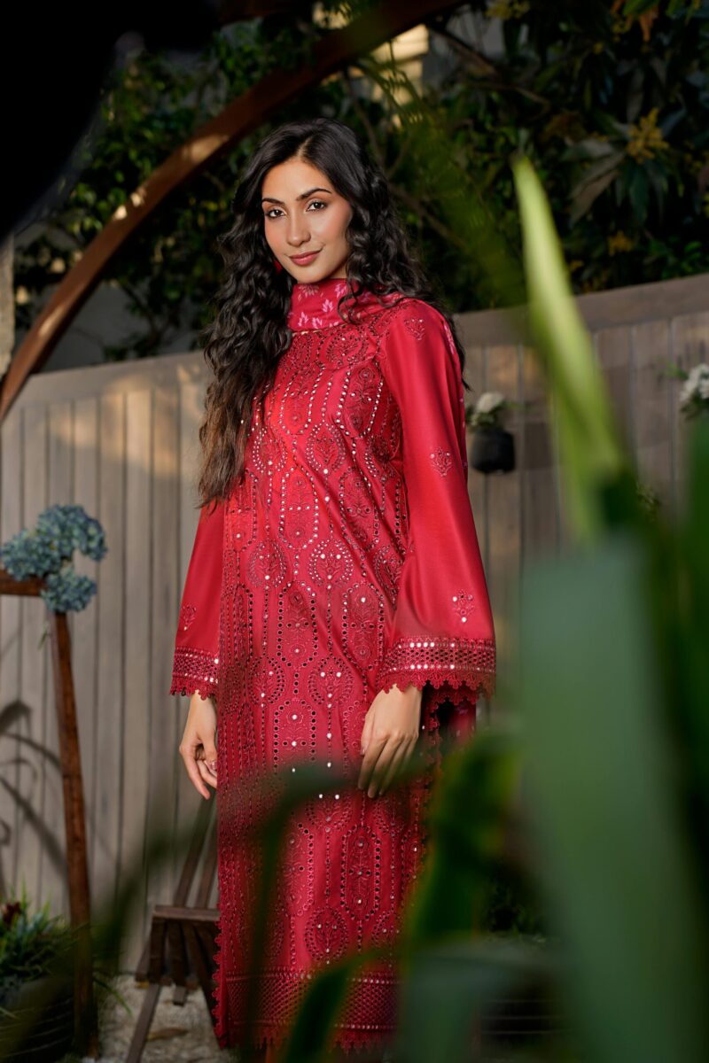 A woman in a stylish, embroidered red dress poses gracefully outdoors in a garden.