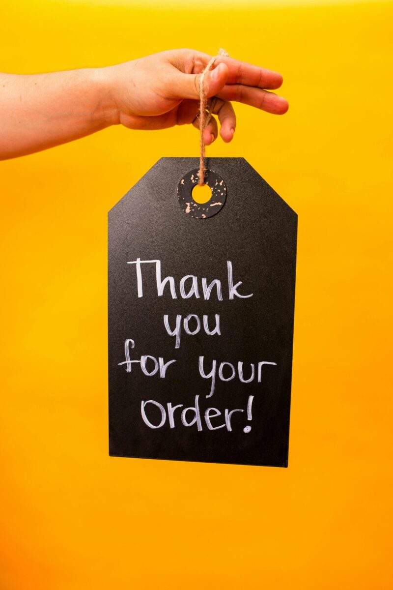 Hand holding a chalkboard with 'Thank you for your order!' written on it, set against a vibrant yellow background.